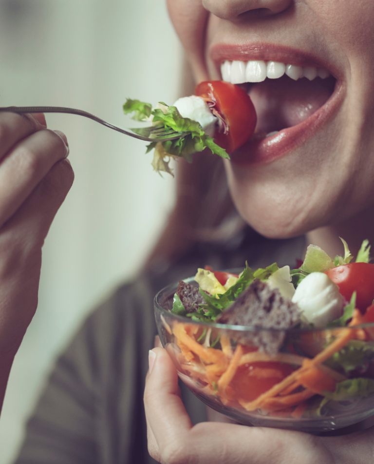 Woman smiling and eating fresh salad with dentures in Kanata from Anata Dental Clinic.